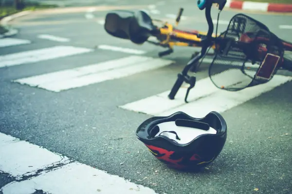 A fallen bicycle lies on a crosswalk, next to a discarded black helmet, suggesting an accident has occurred