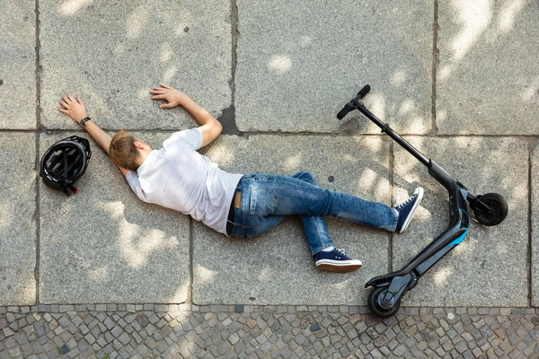 A man lies on the ground beside a scooter, appearing to be resting or recovering from a fall.