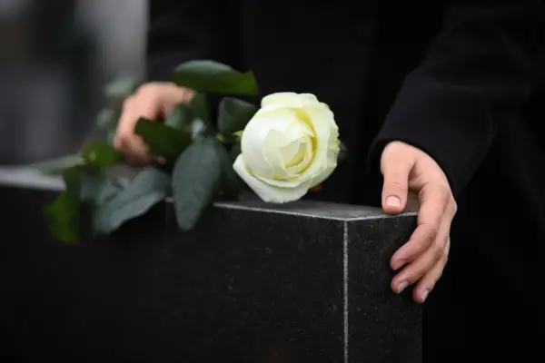 A person gently holds a black granite gravestone, placing a white rose atop it, symbolizing remembrance and mourning