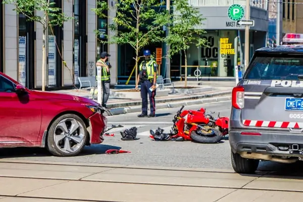 A red car and a motorcycle are involved in an accident, with police investigating the scene and debris scattered on the road.