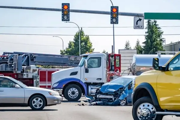 A serious traffic accident at an intersection involving a blue car and a truck, with emergency vehicles responding nearby.